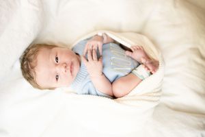 Adorable baby in a light blue knit outfit lying on soft white blankets, gazing upward with bright curious eyes.