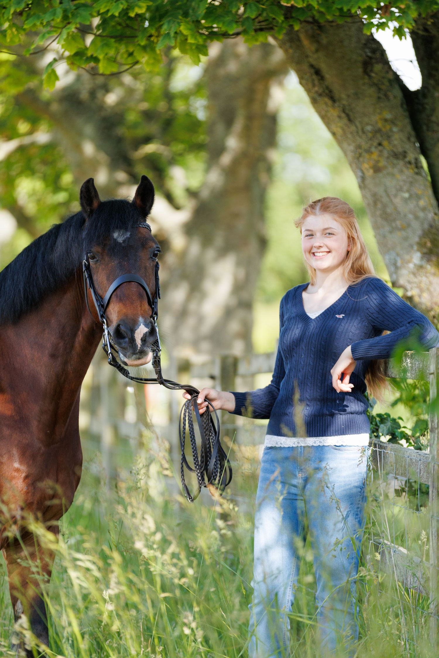 A man and woman smile at a farm gate surrounded by cattle and a horse in a lush green field.