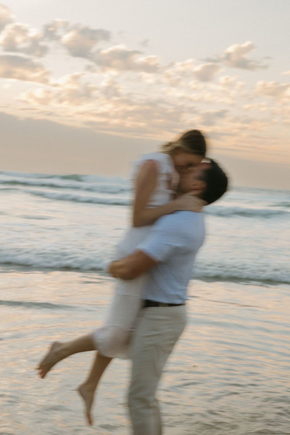 Man lifting woman in romantic embrace on beach at golden sunset with ocean waves.