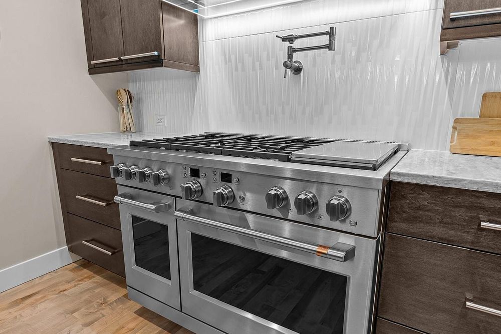 Stainless steel dual-oven professional gas range with dark wood cabinetry and marble backsplash in modern kitchen.