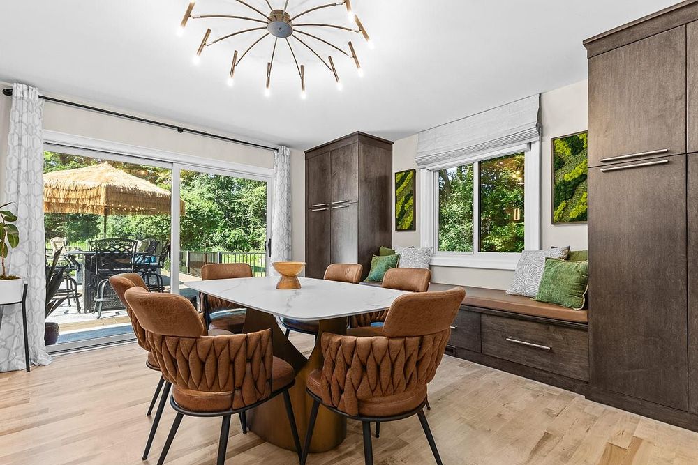 Modern dining room with brown leather chairs, white oval table, built-in bench seating, and sliding doors to a lush backyard.