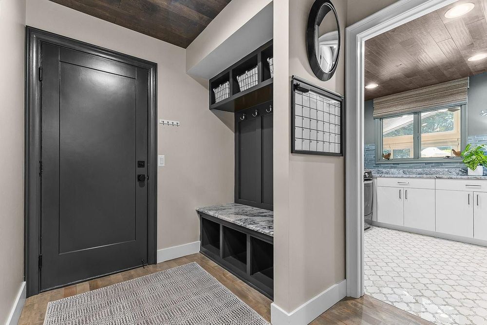 Modern mudroom with black built-in lockers, bench, round mirror, and view into white kitchen.