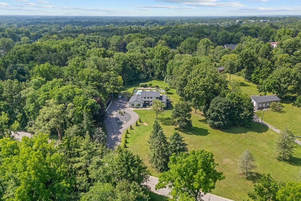 Aerial view of a secluded estate surrounded by lush green trees with a circular driveway and manicured lawn.