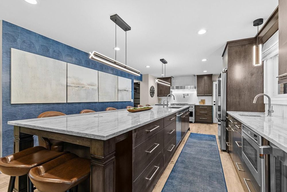 Modern kitchen with dark wood cabinets, marble island, blue tile backsplash, pendant lights, and leather bar stools.