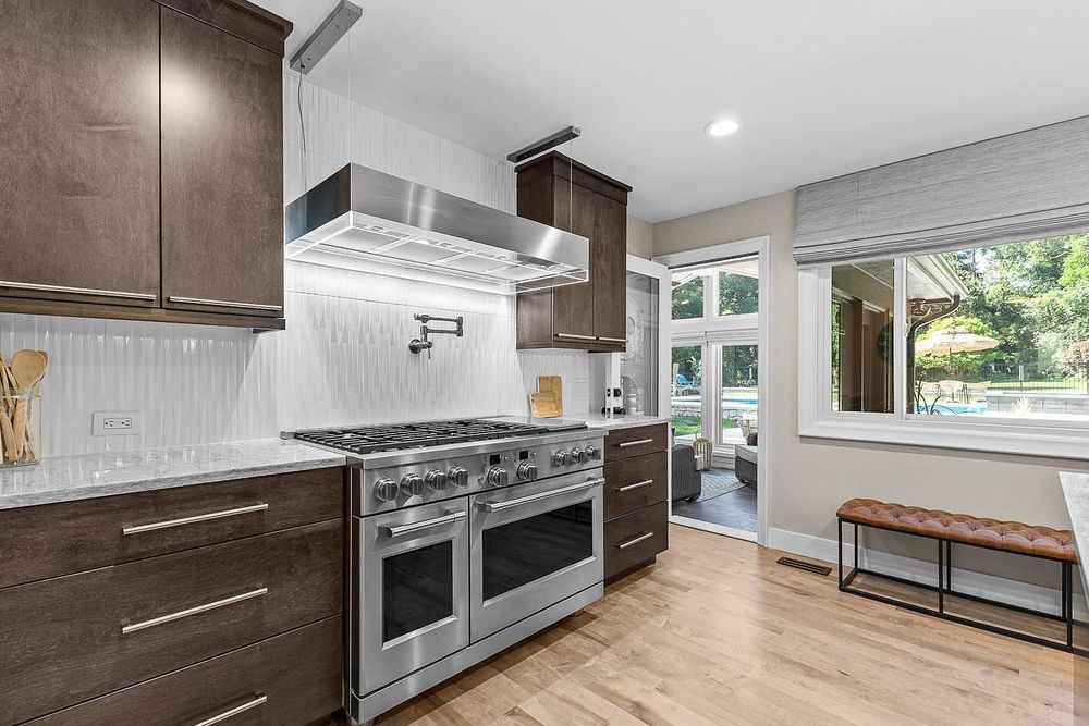Modern kitchen with dark wood cabinets, stainless steel double oven range, white tile backsplash, and light hardwood floors.