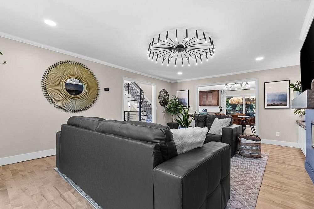 Modern living room with gray leather sofa, decorative mirror, and stylish chandelier over light hardwood floors.