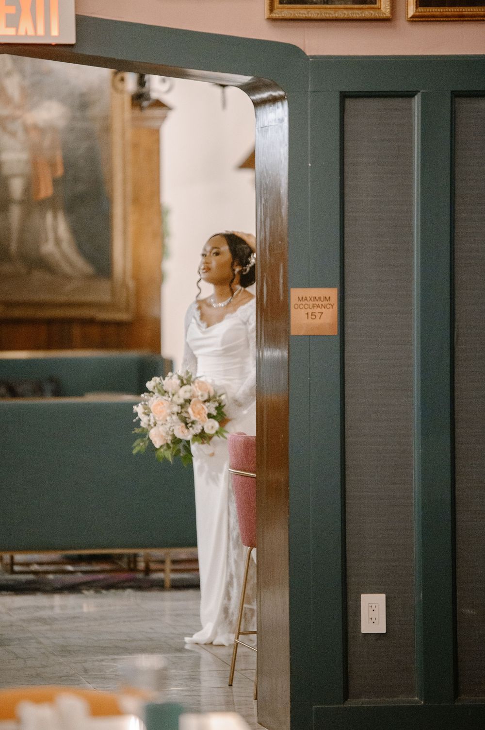 Elegant bride in white gown holds pink bouquet while standing in doorway of a classic venue.