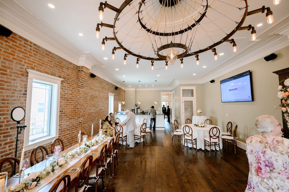 Elegant wedding venue with exposed brick walls, large chandelier, long decorated dining table, and hardwood floors.