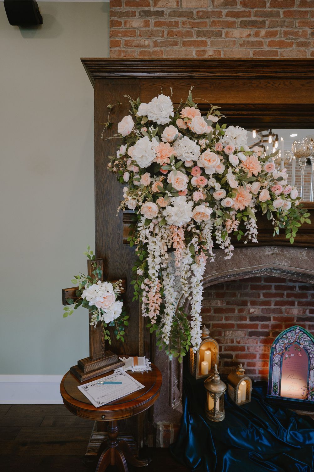 Elegant wedding fireplace display with blush and white floral arrangement, candles, and guest book on wooden table.