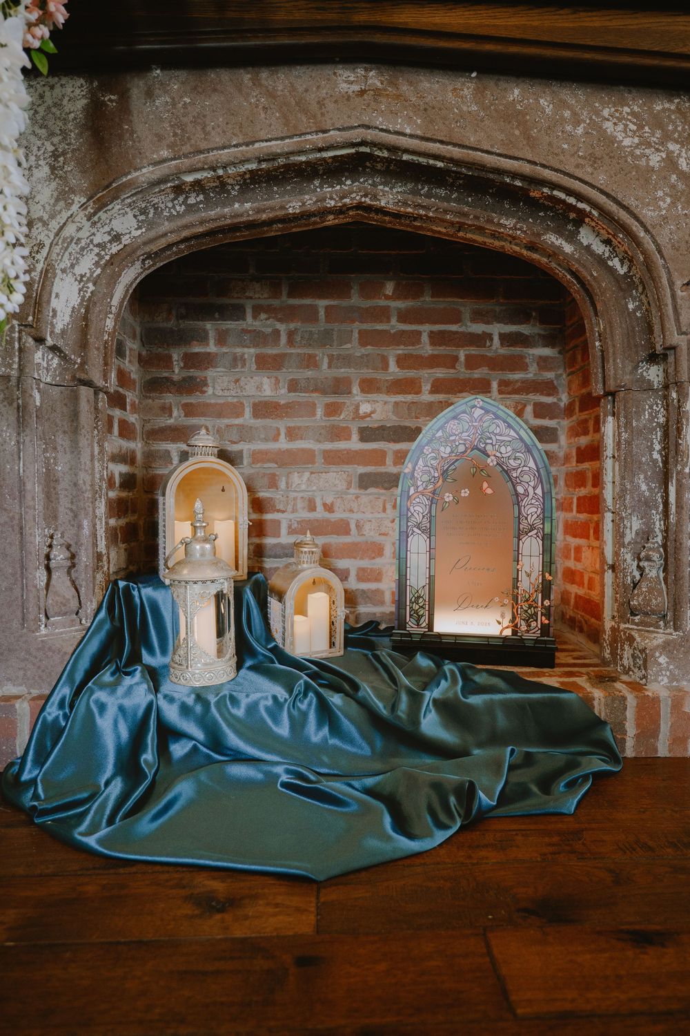 Ornate stone fireplace decorated with lanterns and teal silk fabric for a wedding ceremony.
