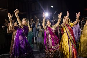 Women in vibrant traditional Indian attire dance with raised hands at a colorful cultural celebration.
