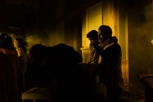 People gathered in a dimly lit outdoor scene with dramatic yellow-green smoke and shadows at night.