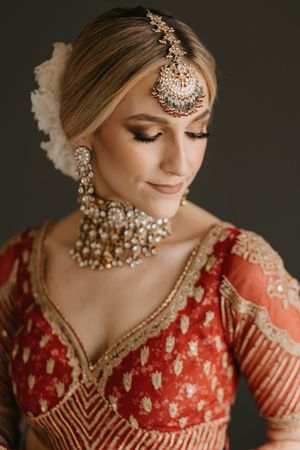 Bride in red lehenga with gold embroidery, wearing kundan jewelry and maang tikka, with elegant bridal makeup.