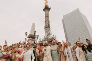 Large group celebrating at Angel of Independence monument in Mexico City, wearing colorful Indian wedding attire.