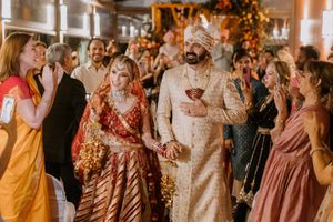 Indian bride and groom in traditional wedding attire walk through guests during a vibrant Hindu wedding ceremony.