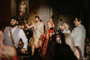 Couple in traditional Indian wedding attire walks down the aisle as guests applaud in an elegant venue.