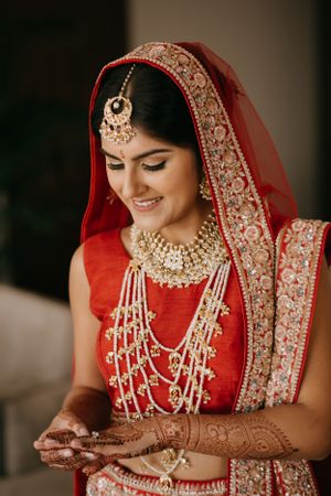 Close-up details of bridal jewelry and henna adorned hands with intricate gold necklaces and red wedding attire.