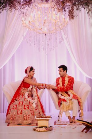 Wedding ceremony setup with white drapes, crystal chandeliers, and couple performing traditional rituals.