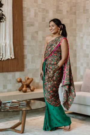 Woman in floral one-shoulder dress poses in modern interior with neutral decor.