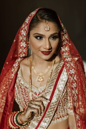 Close-up details of traditional Indian bridal jewelry and makeup with red dupatta.