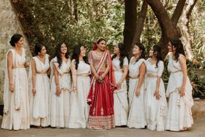 Wedding party in coordinated white outfits posed outdoors for group photo.