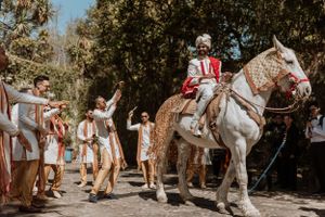 A decorated white horse with traditional ceremonial attire stands while guests gather around during an outdoor celebration.