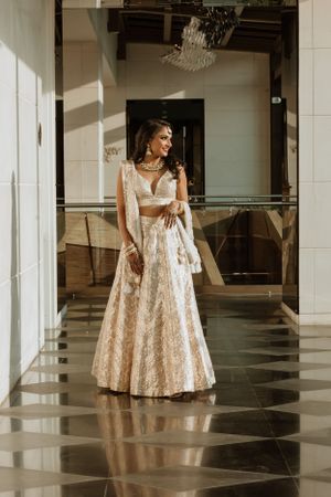 Elegant bridal attire featuring an embroidered cream lehenga photographed in a modern interior setting.