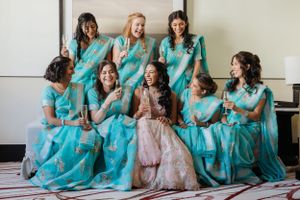 Bridesmaids in matching turquoise saris gather around a bride in pink for a formal wedding photo.