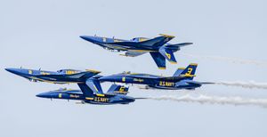 Four U.S. Navy Blue Angels jets fly in close formation, trailing white smoke against a clear sky.