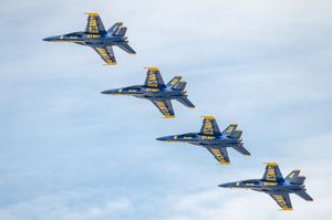 Four Blue Angels F/A-18 Hornets fly in tight diamond formation against a cloudy sky at an airshow.