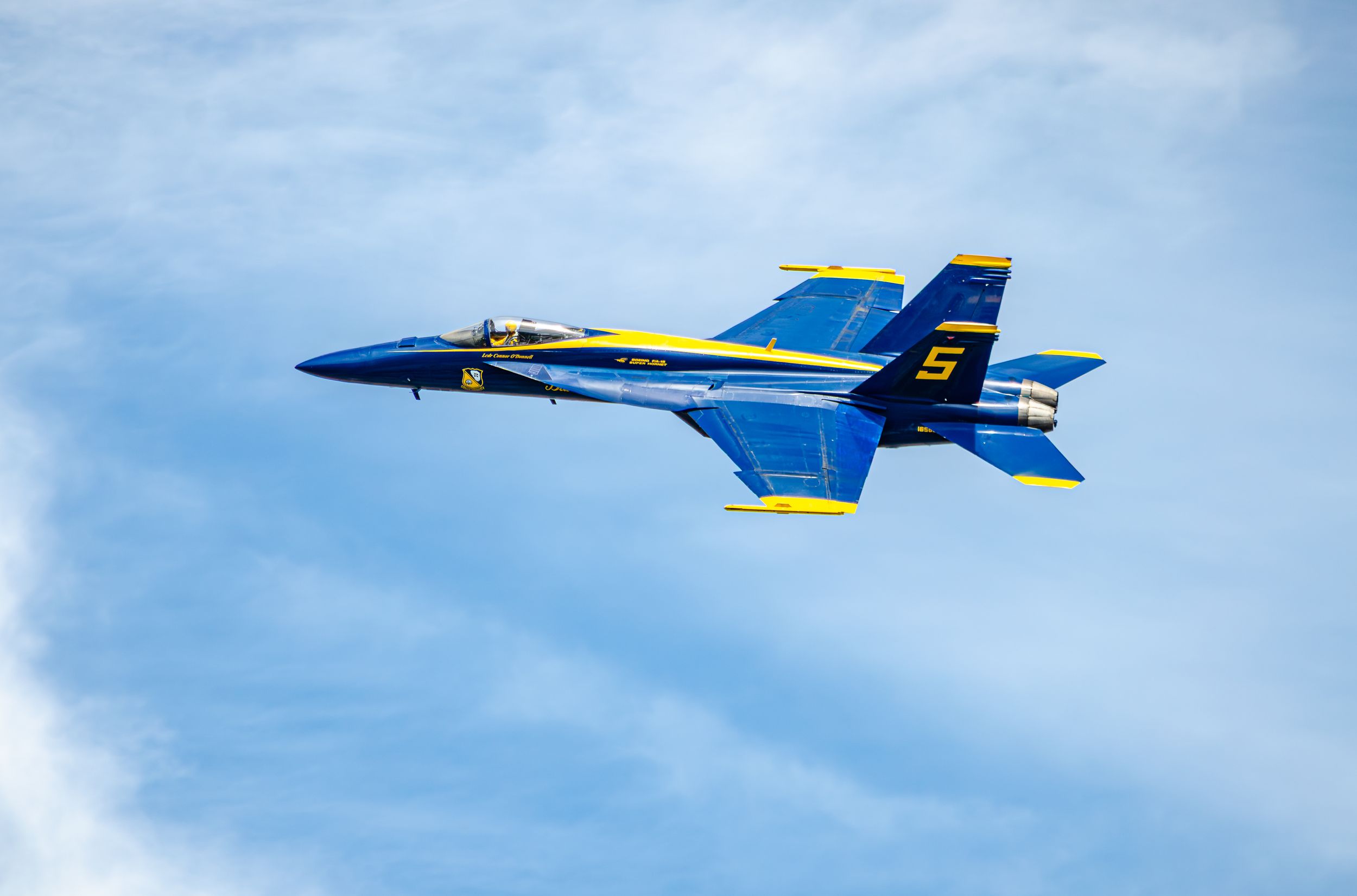 Blue Angels F/A-18 Hornet jet number 5 performing aerobatic maneuver against blue sky.