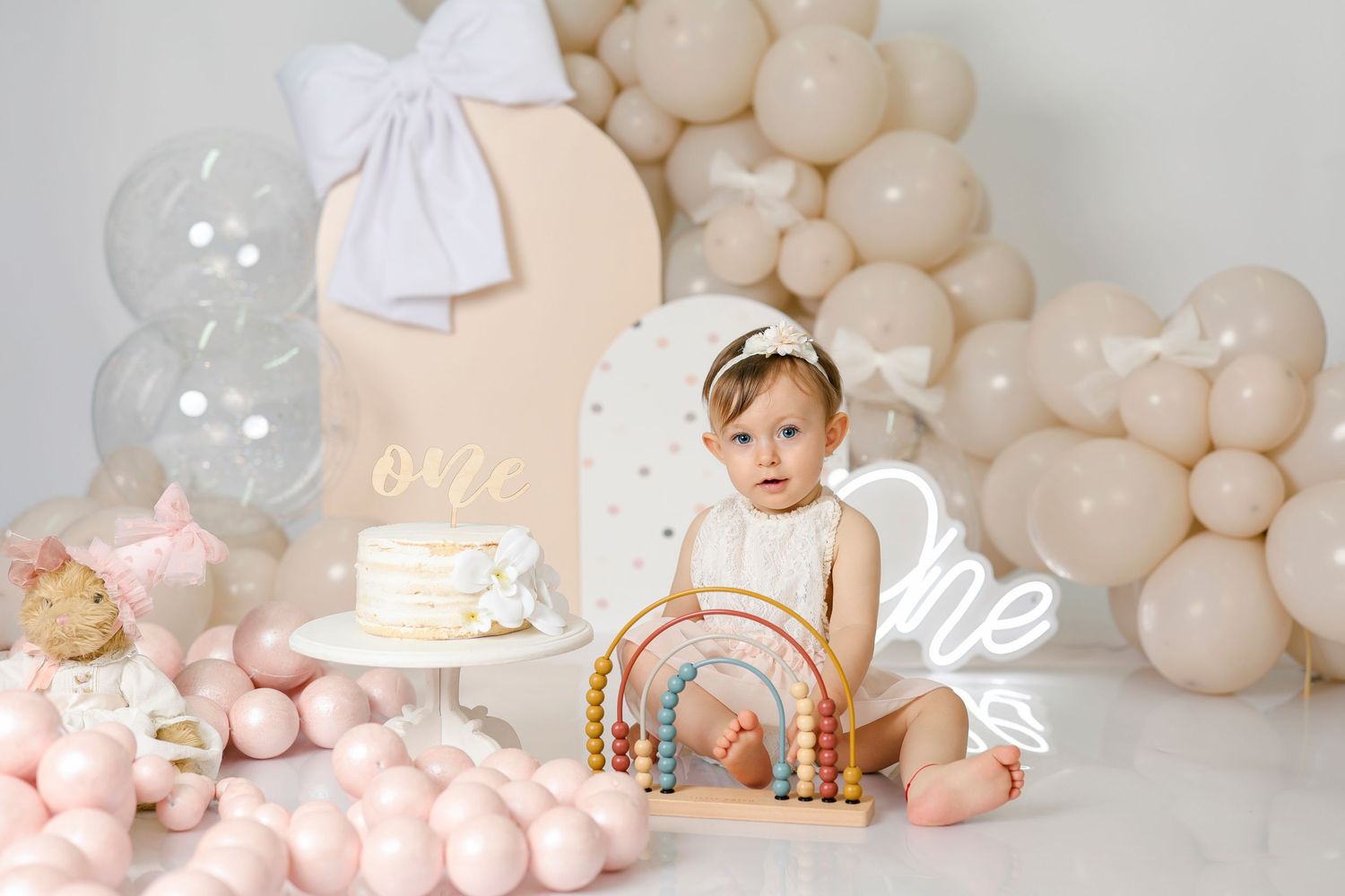 First birthday cake smash setup with pastel balloons and decorations in white and pink tones.