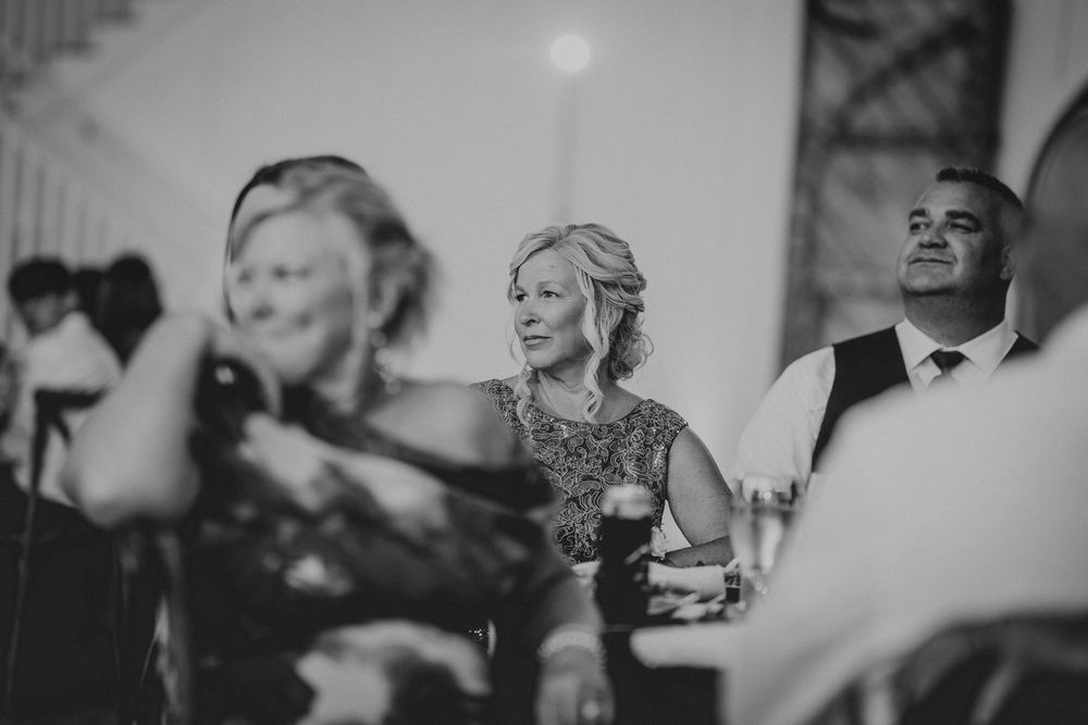 Black and white wedding reception photo of smiling guests enjoying celebrations at an elegant indoor venue.