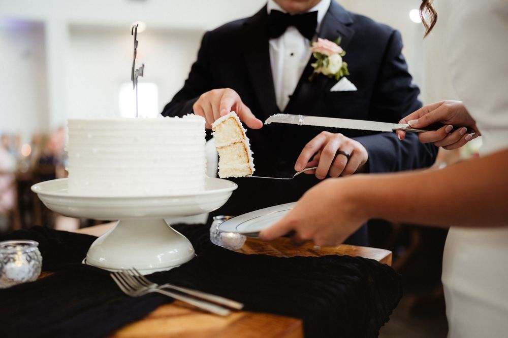 Bride and groom cutting a white wedding cake together at their reception ceremony.