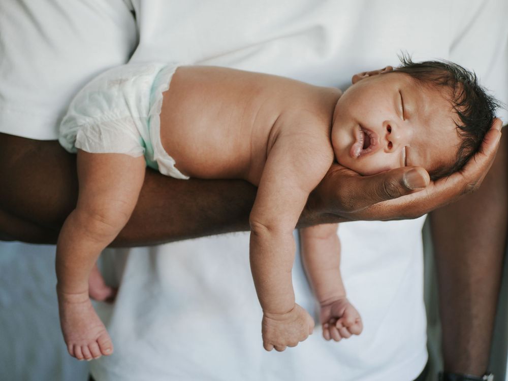 Newborn baby in diaper resting on parent's forearm with eyes gently closed.