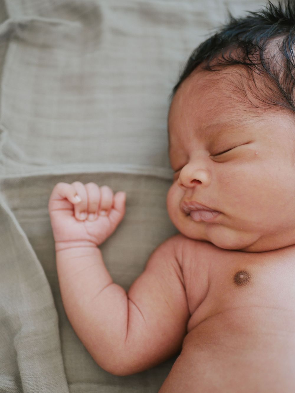 Peaceful newborn baby sleeping on a soft green blanket with tiny fist raised.