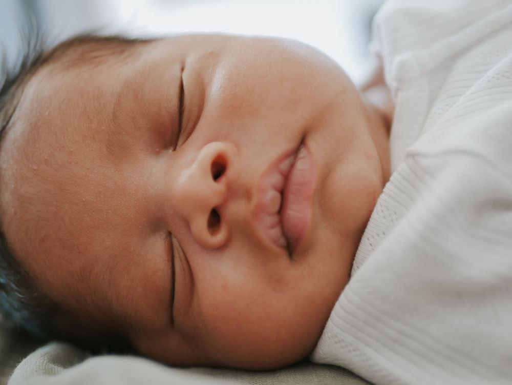 Close-up of a sleeping newborn baby with dark hair and a gentle smile.