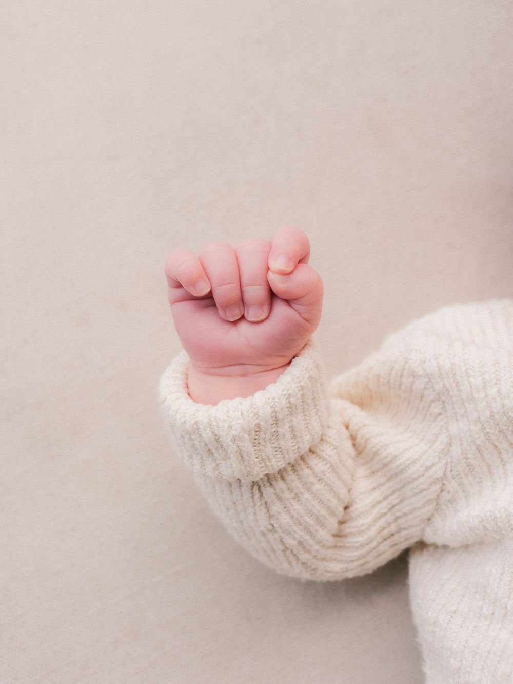 Close-up of a newborn baby's tiny fist in a cream ribbed knit sweater.
