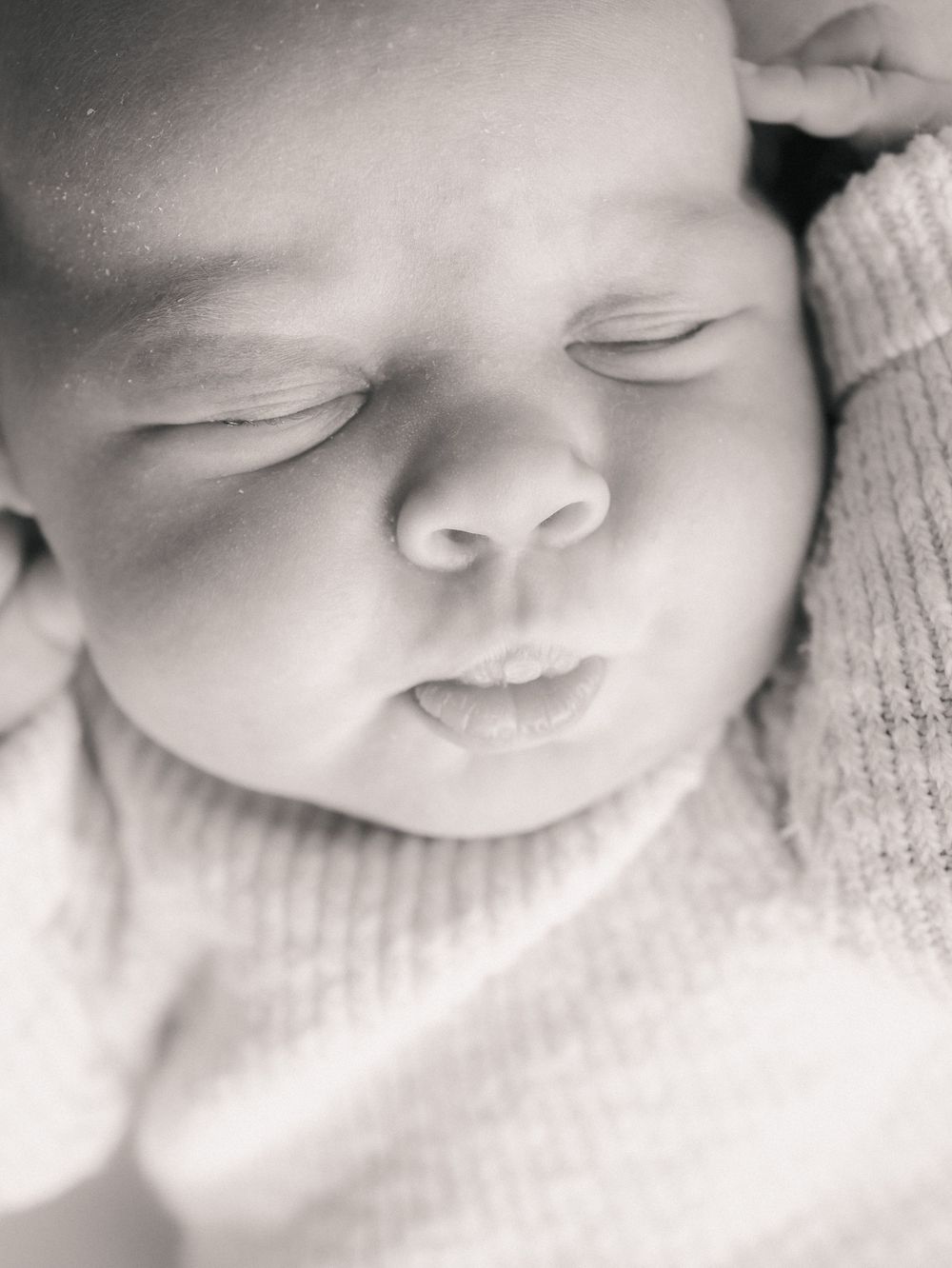 Black and white close-up portrait of a sleeping newborn baby in soft knitwear.