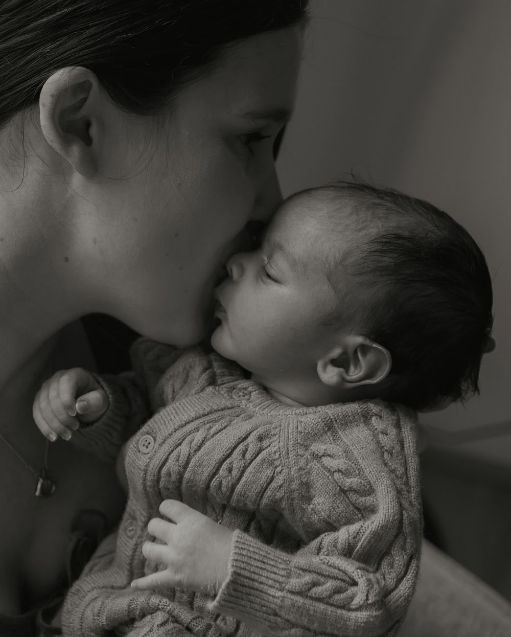 Black and white photo of mother gently kissing her sleeping newborn baby.