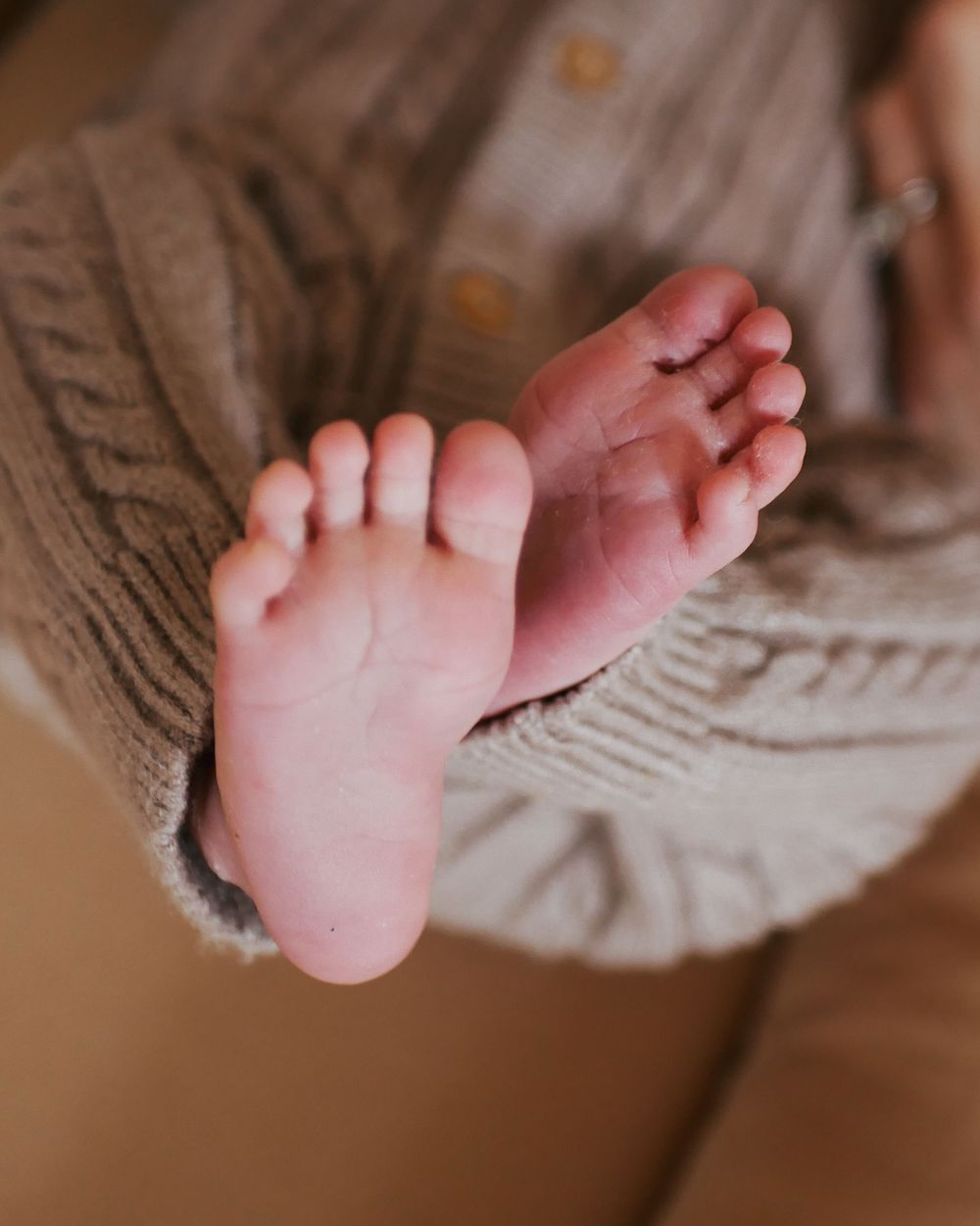 Close-up of tiny newborn baby feet peeking out from a soft knit sweater.