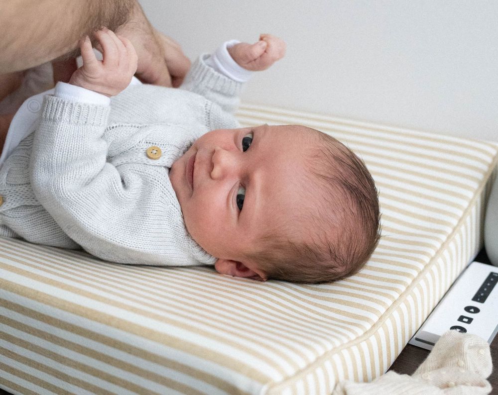 Newborn baby in grey knit outfit lying on striped changing mat.
