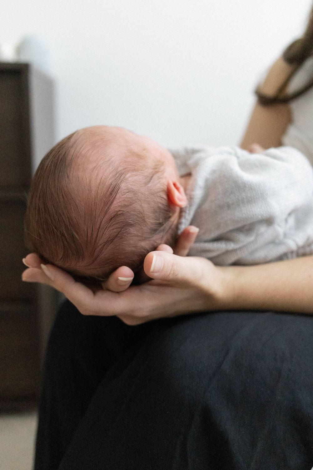 Close-up of newborn baby cradled in mothers hands wrapped in grey swaddle.