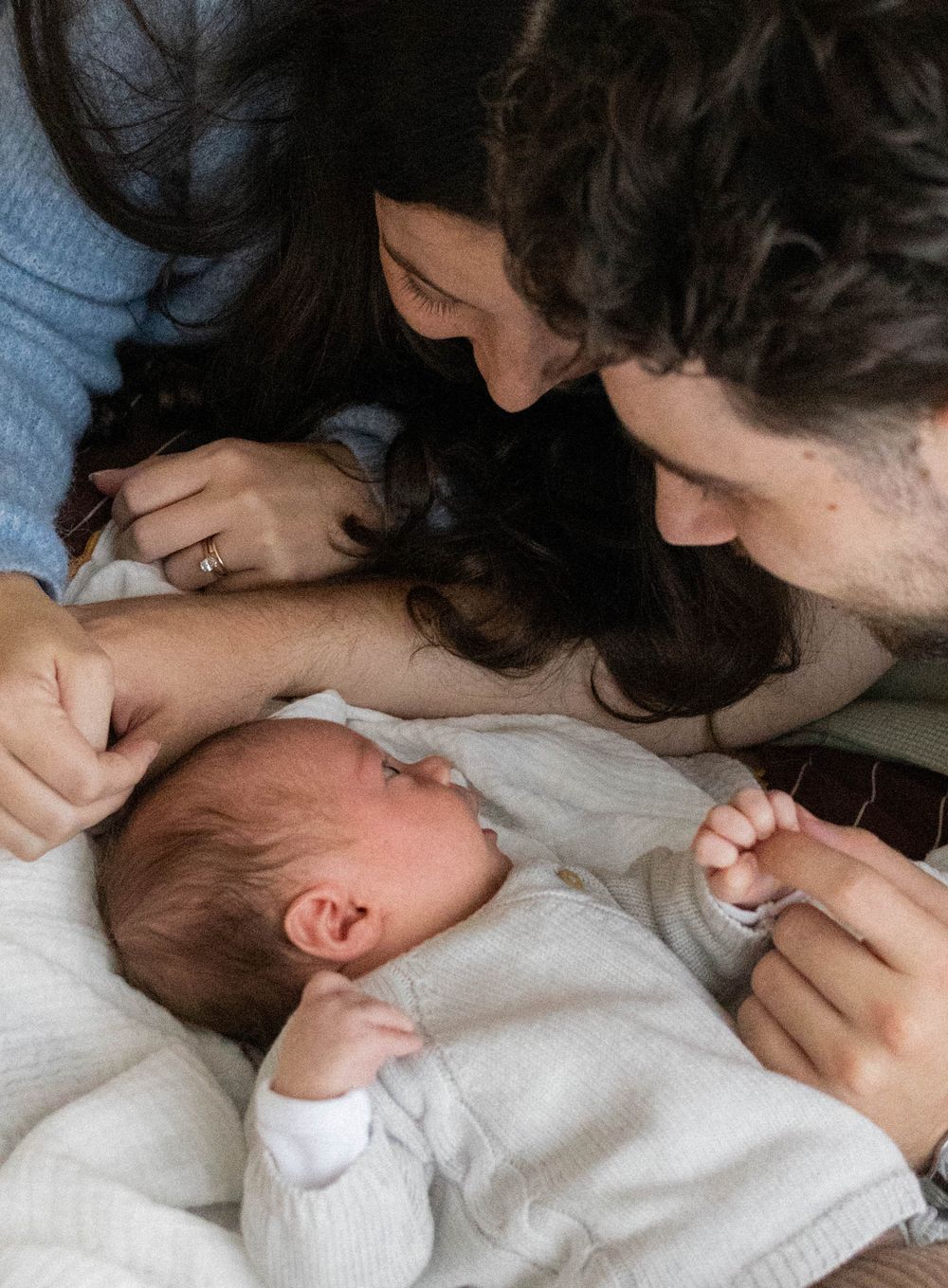 New parents lovingly gaze at their sleeping newborn baby lying between them.