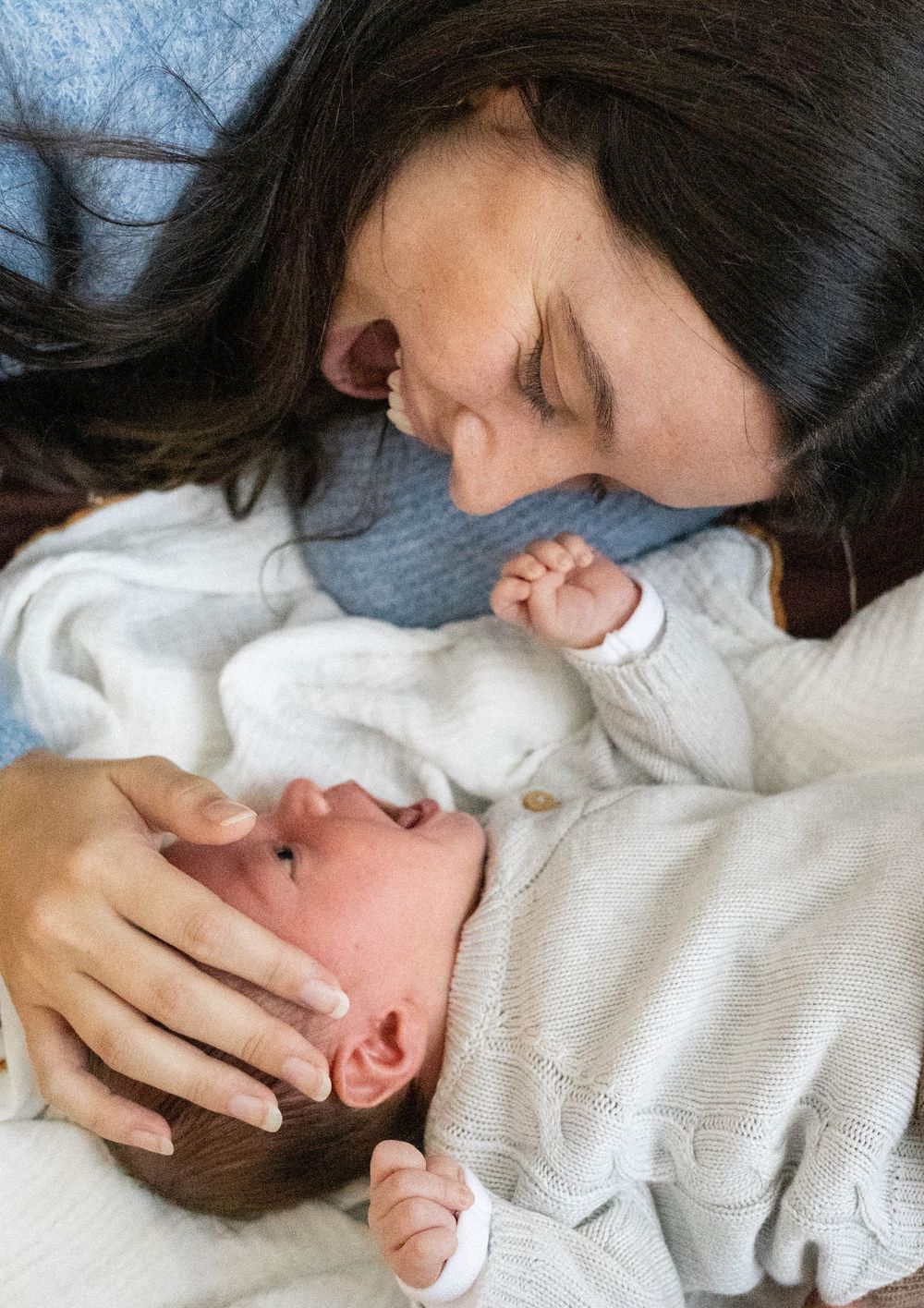 Mother tenderly kisses her newborn baby while cradling their tiny face in her hand.