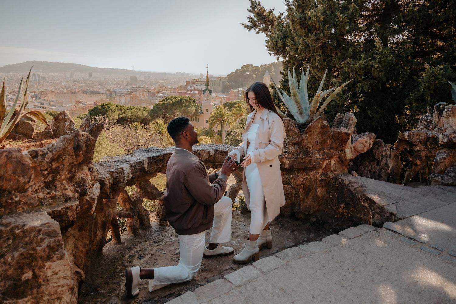 Barcelona surprise proposal photoshoot. A man kneels with a ring at Park Güell while his partner reacts with joy.