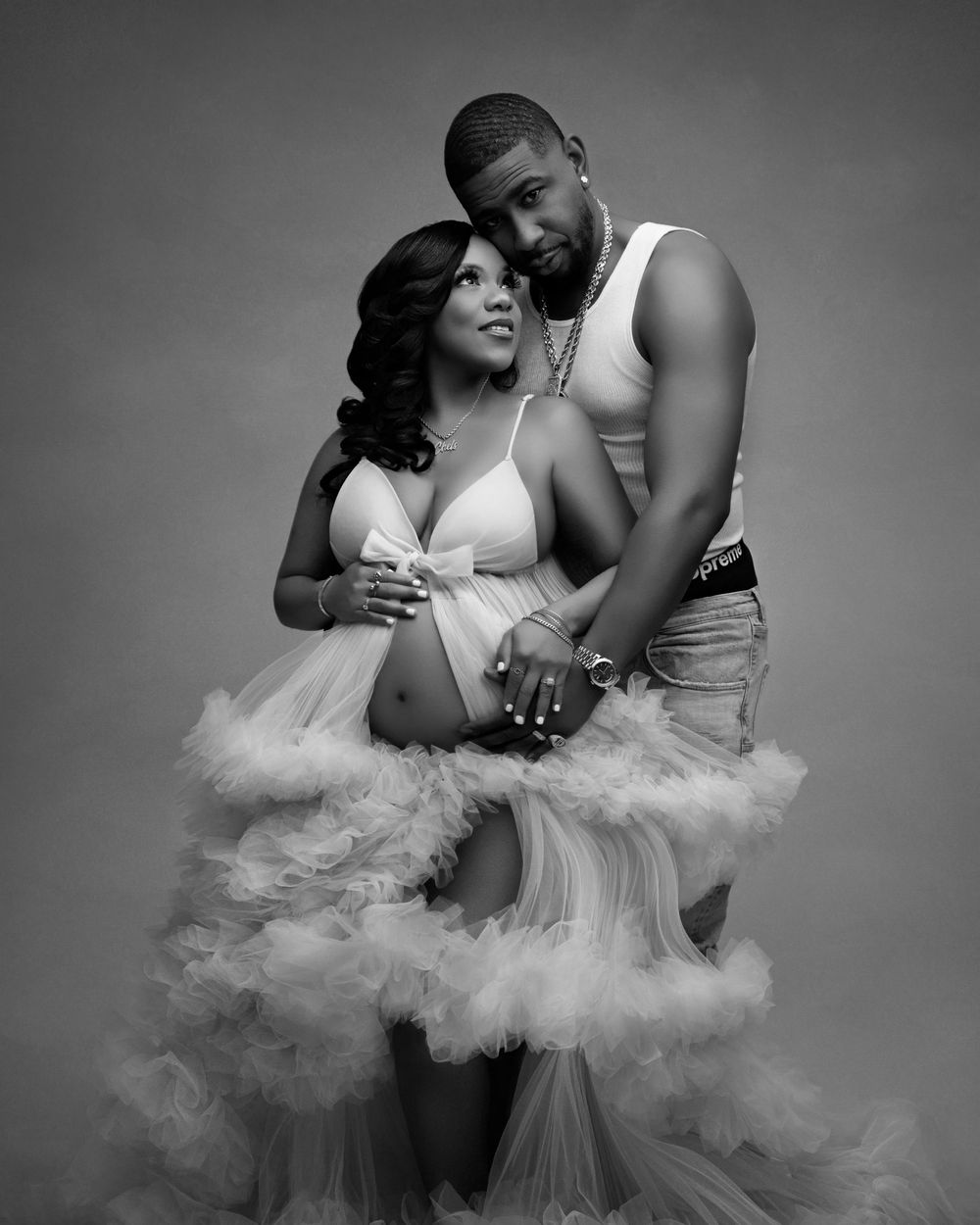 Black and white maternity photo of a couple, woman in a flowing tulle gown cradling her baby bump.