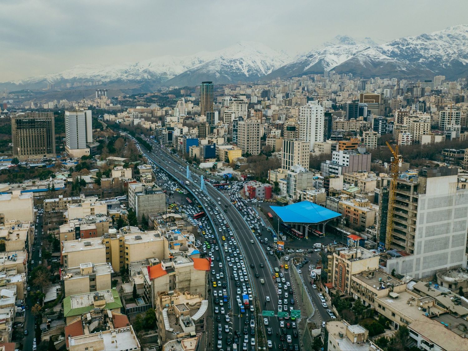 Aerial view of Tehran, Iran, with a busy highway through the city and snow-capped mountains behind.