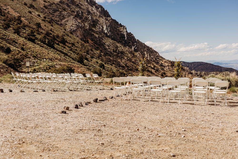 Outdoor wedding ceremony setup with white chairs arranged in rows on rocky terrain with mountain backdrop.