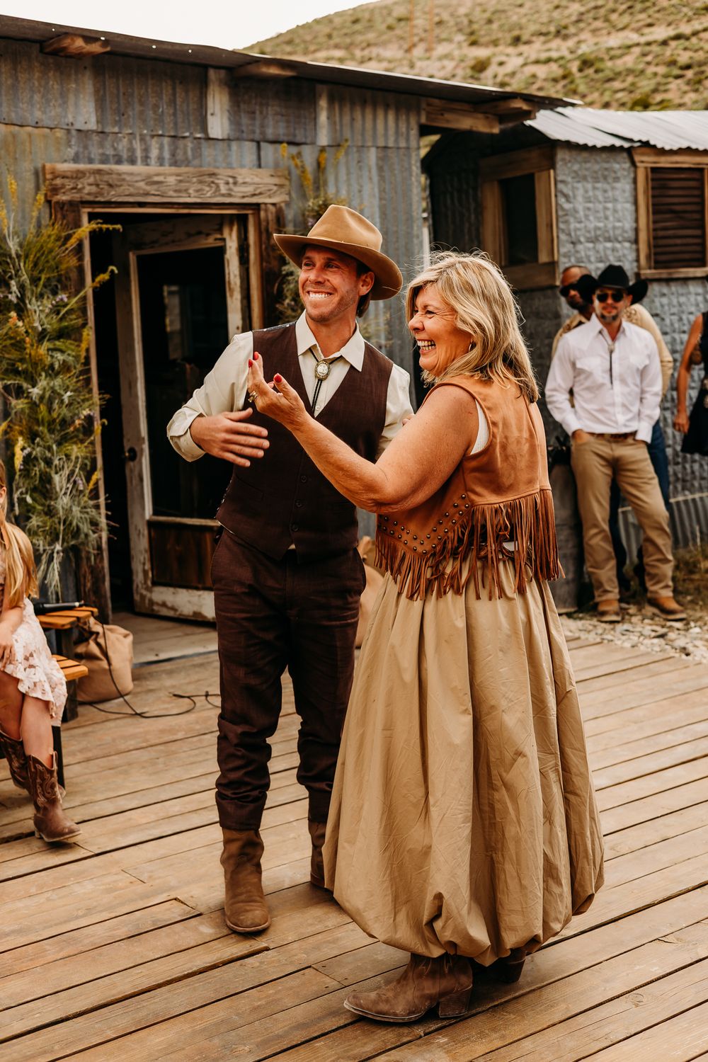 Two people in Western attire dance on a wooden deck at an outdoor country-themed event.